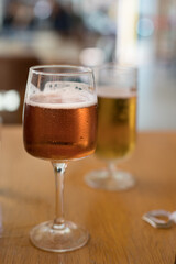 Refreshing cold glass of ale beer with bubbles and drops on a wooden table next to a blurred lager beer.