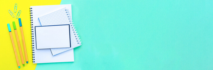 Banner. Stack of notebooks on a spiral overlap. Bright, colorful yellow with mint color background. Back to school concept. Copy space, top view, flat lay.