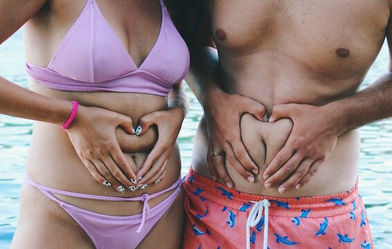Image of body sizes and shapes , two friends holding heart hands around belly button *2