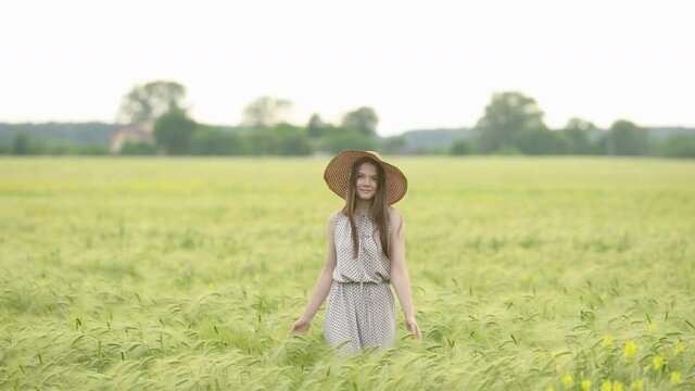Portrait of a young beautiful woman in dress walks through a wheat field at a sunny day. Happy free girl run in park agricultural land. Freedom concept.