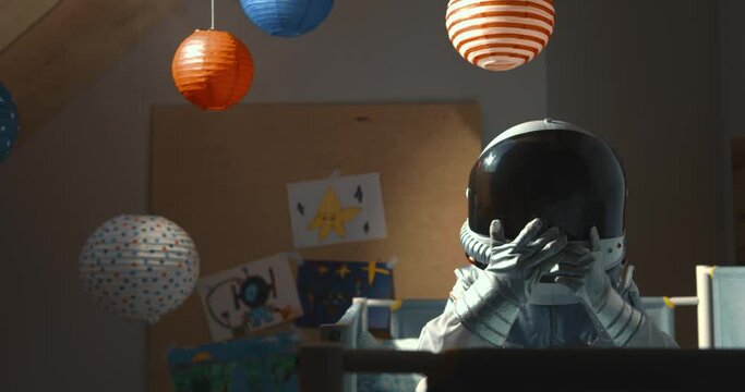 Dreaming about space travel. Little astronaut child sits on bed going to sleep in his room wearing space suit and helmet