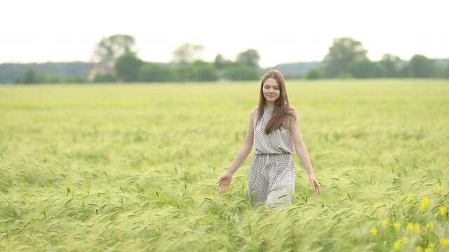 Portrait of a young beautiful woman in dress walks through a wheat field at a sunny day. Happy free girl run in park agricultural land. Freedom concept.