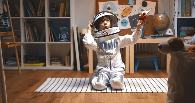 Happy cute little boy child in astronaut suit playing space ship pilot, flying rocket toy sitting on the floor in room.