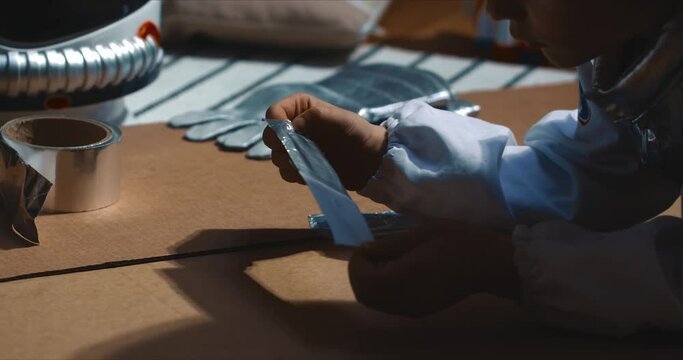 Cinematic close-up, hands of child playing space pilot, having fun sticking cardboard pieces with silver scotch tape.