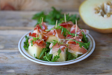 Melon jamon appetizer on a plate. Melon prosciutto salad on skewers.