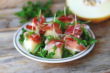 Melon jamon appetizer on a plate. Melon prosciutto salad on skewers.