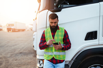 Young handsome bearded man standing in font of his truck and using phone.