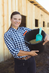 Horse owner holding a bucket full of grains and a scoop.horse feeds. girl in the horse ranch with...