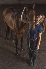 Horsewoman embracing her seal brown horse in the stable. Girl holding the stallion's rope and expressing her love. Bonding between human beings and horses concept. Love for horses.