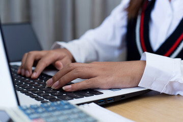Young woman sitting, using laptop, tablet, notebook and calculator working from home. Closeup shot of unrecognizable woman, hands working on computer keyboard. 