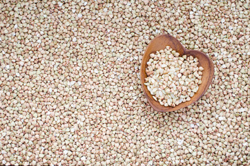 Dry organic buckwheat seed pile in heart shape wooden bowl on buckwheat background. Concept of natural cereal and grain seed or agricultural product concept