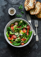 Delicious Mediterranean style salad with salmon, egg, vegetables, lettuce and grilled bread on a dark background, top view