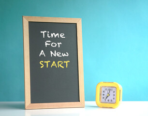 Time for a new start, phrase on blackboard. Next to a yellow alarm clock. On blue background.