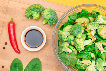 Fresh Green Salad of Avocado, Broccoli, Spinach and Cucumber with Soy Sauce and Red Hot Pepper on Wooden Cutting Board. Vegan Salad. Vegetarian Culture. Raw Food. Healthy Eating and Vegetable Diet