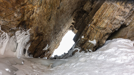 There is a narrow sloping passage in the granite rock. There are cracks on the stones. Icicles on the base of the cliff. Sepia shades. Baikal. Siberia