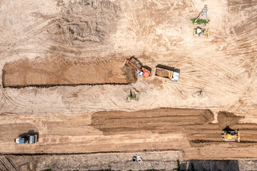 heavy industrial machines working on construction site. bulldozer and road rollers is leveling and compacting soil. excavator is loading soil into a dump truck. industrial area from drone view.