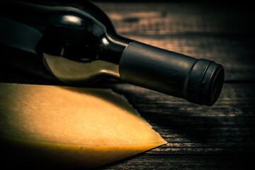 Bottle of red wine with a piece of parmesan lying on an old wooden table. Close up view, focus on the bottle of red wine