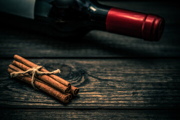 Bottle of red wine and cinnamon sticks tied with jute rope lying on an old wooden table. Close up view, focus on the cinnamon sticks