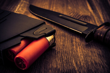 Magazine with red cartridges 12 gauge and combat knife on the wooden table. Close up view