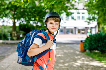 Happy little kid boy with satchel and bicycle helmet. Schoolkid on the way to middle or high school. Healthy adorable child outdoors on school yard. Back to school. Building on background.