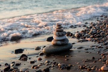 Pyramid of stones on the beach at sunset, beautiful seascape, rest and seaside vacation concept. 