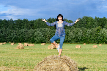 Naklejka na ściany i meble The girl in blue is engaged in yoga. Relax in nature. The girl stands with one foot pressed on the hay. Unity with nature.