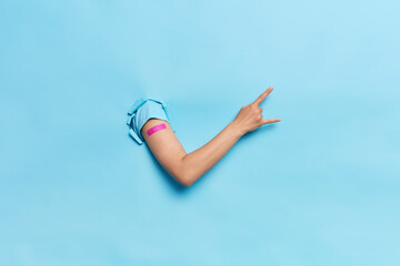 Vaccination against coronavirus. Unrecognizable human breaks arm through paper blue background...