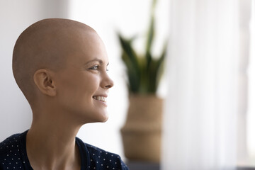 Side view head shot close up smiling beautiful young woman with bald after chemotherapy head...