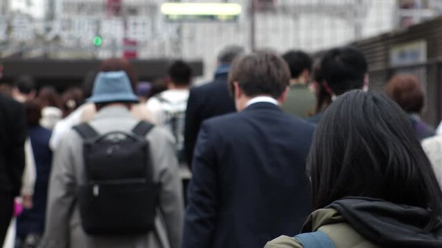 OSAKA, JAPAN - APR 2021 : Back shot of crowd of people walking down the street. View of many commuters after work near the station. Slow motion shot. Japanese city lifestyle concept.