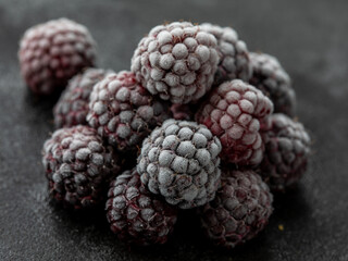 heap of frozen black berry dewberry fruits on dark background, close up, side view, horizontal.
