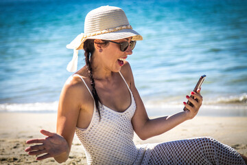 woman with surprise gesture on the beach with mobile phone