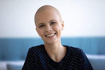 Head shot portrait of smiling young sincere hairless after chemotherapy woman, feeling optimistic in cancer fight. Joyful laughing candid millennial bald lady with inner strength looking at camera.