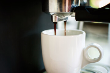 Hot coffee dropping into the coffee cup by coffee machine.