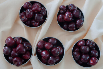 Five small bowls full of ripe delicious red cherries on the beige background, top view.