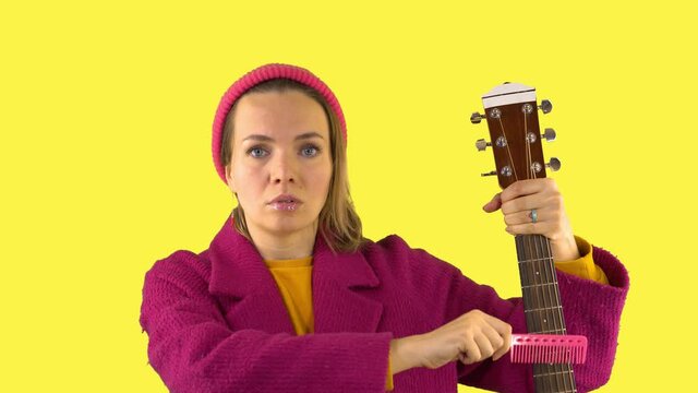 Crazy Woman with Strange Look, Pink Comb Combing Guitar, Surrealism on Yellow Background. Psychopath, Guitar Tuning, Advertising Concept