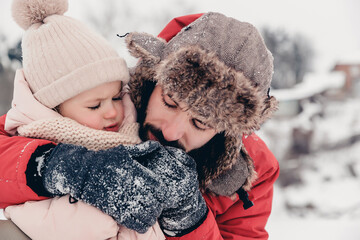 Handsome bearded young dad and his little cute daughter are having fun outdoor in winter. Family concept. The father warms the handles of the daughter who froze from the frost