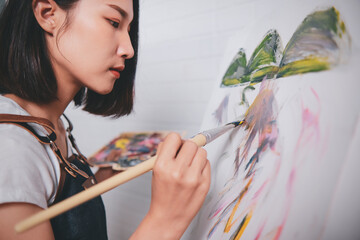 Asian woman artist painting picture with blank canvas side view, using paint brush and colour pallets having fun creativity activity occupation hobby concept, creative thinking imagination visual - obrazy, fototapety, plakaty