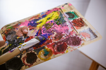close up artist painting picture with blank canvas side view, using paint brush and colour pallets having fun creativity activity occupation hobby concept, creative thinking imagination visual