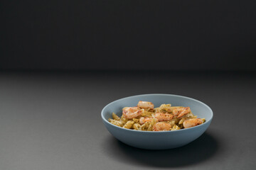 Penne pasta with shrimps and pesto in blue bowl with copy space