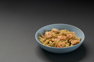 Penne pasta with shrimps and pesto in blue bowl with copy space