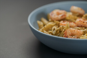 Penne pasta with shrimps and pesto in blue bowl with copy space