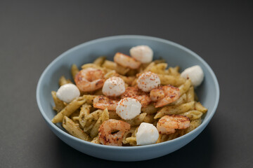 Penne pasta with shrimps and mozzarella and pesto in blue bowl