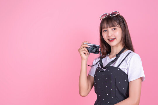 Happy smiling attractive Asian girl with braces tourist with camera taking pictures in summer dress sunglasses, summer holiday vacation tourist traveling abroad bag adventure, pink isolated background