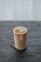 Ice coffee wih milk in tumbler glass on black oak table