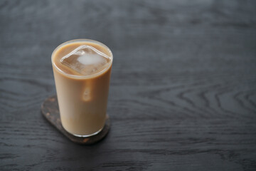 Ice coffee wih milk in tumbler glass on black oak table