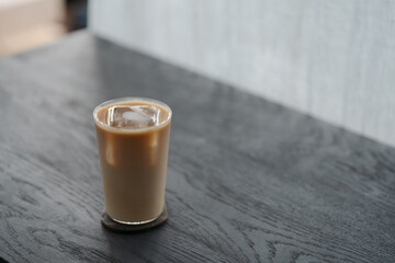 Ice coffee wih milk in tumbler glass on black oak table