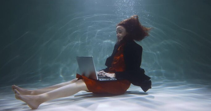 Freelance work concept. Young happy attractive sales expert business woman using laptop working under water slow motion.