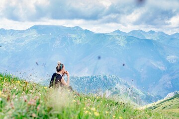 A blonde hiker sits on the grass, eats and drinks water, resting in the beautiful Polish mountains. Tatra Mountains.