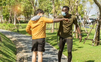 Asian man greets an African-American friend wearing a coronavirus mask, goes jogging in the park together in the morning and bumps his elbows to greet each other.New normal concept.