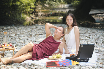 a girl and a woman in nature listen to music and eat fruit